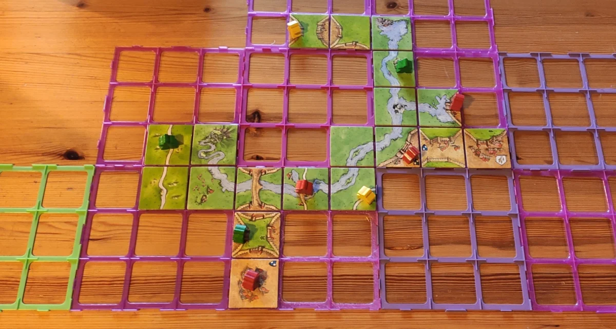 vasemmassa reunassa carcassonne-paloja aseteltuna, pääosan kuvasta täyttää eriväriset ruudukot, joihin mahtuu pelilaatta
