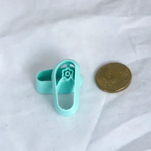 flipflopleikkuri, jossa varpaiden väliin tulee kuusilehtisen kukan kuvio, oikealla 20snt kolikko mittakaavana