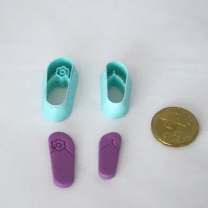 ylärivissä vasemmalla flipflopleikkuri, jossa varpaiden väliin tulee kuusilehtisen kukan kuvio, oikealla tavallinen flipflopleikkuri. Leikkureiden alapuolella askartelumassasta leikatut kuviot. oikeassa reunassa 20snt kolikko antamassa mittakaavaa